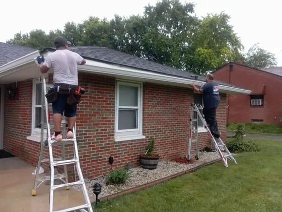 Two KSG installers on ladders fitting gutter to a brick ranch
